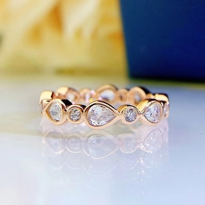Primer plano de anillo en oro rosa con piedras de gota y diseño ondulado elegante