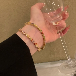 Dettaglio di un set di bracciali con strass arcobaleno dorati indossati con eleganza