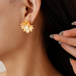 Detailed view of matte gold daisy earrings with a sparkling central crystal on a model