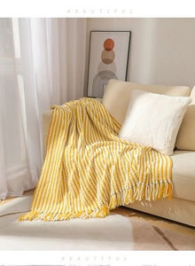 Detail of yellow and white striped knitted throw blanket with tassels on a cozy sofa