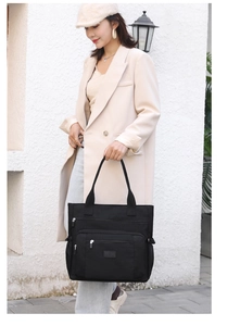 Gros plan sur un grand sac cabas noir avec poche zippée porté par un mannequin en manteau