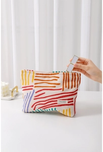 Detail of floral corduroy makeup bag showing hand placing lipstick inside for storage