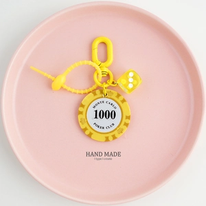 Detail view of a yellow poker chip keychain with a translucent dice and a plastic carabiner