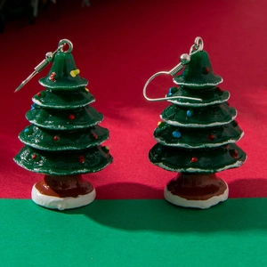 Detail view of green Christmas tree earrings with colorful ornaments on festive background