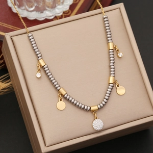 Two-tone beaded stainless steel necklace with gold circular charms on a jewelry box