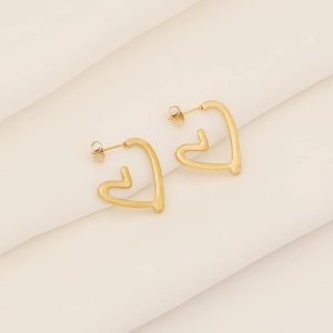 Minimalist gold hollow heart stud earrings in stainless steel on white fabric background