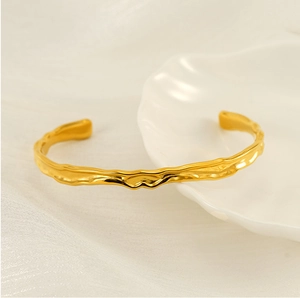 Dettaglio del bracciale dorato in acciaio inossidabile con texture lava su piatto a conchiglia