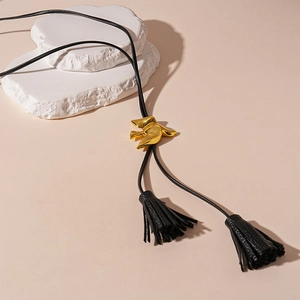 Detailed macro of golden bird slider with black tassels on minimalist leather cord necklace