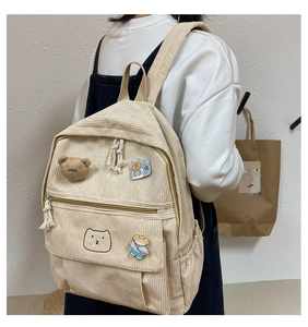 Detalle de mochila de pana beige con bordado de oso y colgante de peluche decorativo