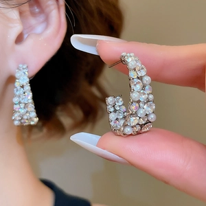 Macro detail of oval C-shaped earrings featuring shimmering pearls and micro-pave diamonds