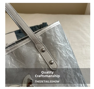 Detail of silver pleated tote bag featuring rabbit metal logo and rivet reinforced straps
