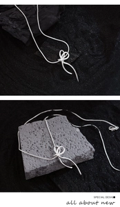 Detailed view of silver bow pendant on snake chain against textured black background