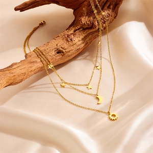 Elegant gold-tone layered necklace featuring celestial star, moon and sun pendants on wood