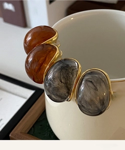 Close-up of retro oval resin earrings with amber and marble patterns on a cup