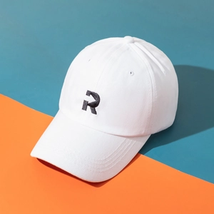 White cotton baseball cap with black embroidered R logo on a modern color-block background