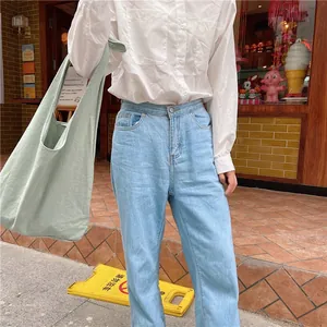 Detail view of light green canvas tote bag paired with light blue high waist straight jeans