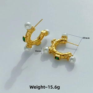 Macro detail of gold C-shaped earrings with irregular texture, pearl, and emerald zircon