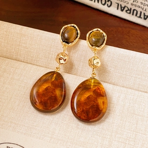 Boucles d'oreilles pendantes dorées en résine ambre sur un fond vintage minimaliste
