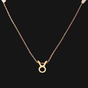 Macro shot of gold Taurus zodiac necklace pendant on minimalist chain with black background