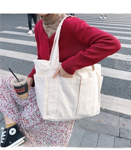 Détail d'un grand sac cabas en toile crème avec plusieurs poches avant pour le quotidien