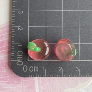 Macro detail of mini 1.5cm pink resin apple charms on a black measurement cutting mat