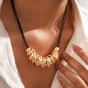 Close-up of gold geometric rings on black cord necklace worn on a female neck