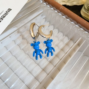 Detail of blue flocked bear charm earring on a clear textured glass and wooden surface