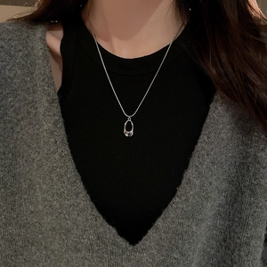 Detail of silver stainless steel necklace with oval pendant and blue-green gemstone on a model