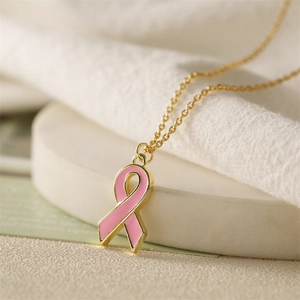 Close-up of pink enamel ribbon pendant on a gold chain over a soft beige background