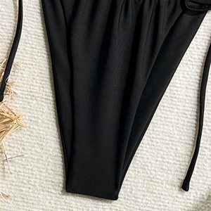 Close-up of black lace-up bikini bottom with matte fabric texture on beige rug