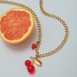 Close-up of golden pearl necklace with red cherry and strawberry fruit charms
