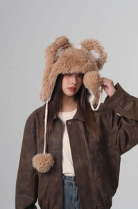 Close-up of khaki plush bucket hat with bear ears and braided straps with soft fur pom-poms