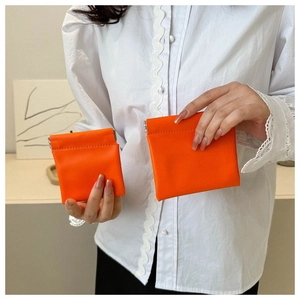 Close-up of orange leather mini coin purses in two sizes held by a hand against white shirt