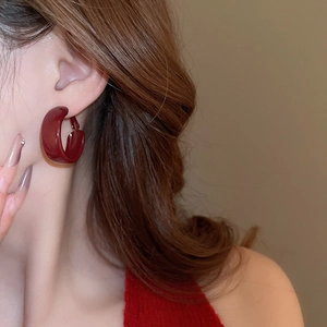 Close-up of deep red glossy C-shaped hoop earrings worn by a model in a retro style