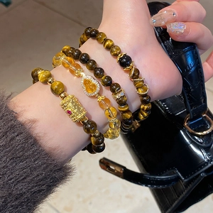 Detail of stacked tiger eye and citrine beaded bracelets with a gold gourd charm on wrist