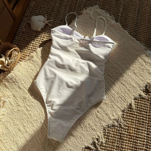 Flat lay of a white one-piece swimsuit with star cutouts on a beach-style decor mat