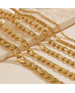 Detail view of various widths of gold-plated Figaro chains on white marble background
