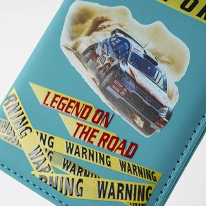 Detailed close-up of blue rally car passport cover, featuring textured leather and warning print.