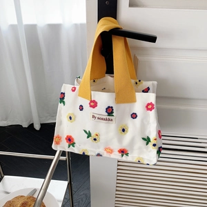 Close-up of canvas lunch bag featuring colorful floral embroidery and yellow handles
