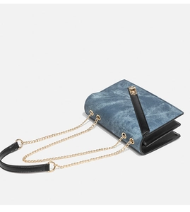 Detail of blue denim shoulder bag showing gold chain strap and accordion side structure