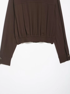 Detail of brown long-sleeve shirt with elastic waist hem and buttoned cuffs close-up