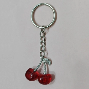 Detailed view of red resin cherry keychain with silver leaves on pink surface