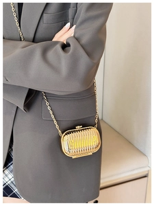 Close-up of golden cylindrical mini crossbody bag with vertical stripes and metal chain