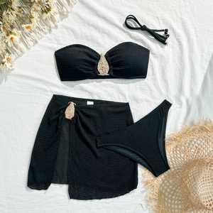 Detail of black bikini with golden metal pendants and textured fabric on white background