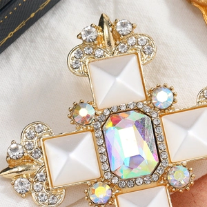 Macro shot of vintage gold cross brooch with rainbow center stone and crystal details
