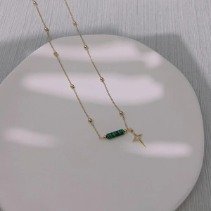 Detailed shot of gold necklace with malachite beads and star pendant on ceramic tray