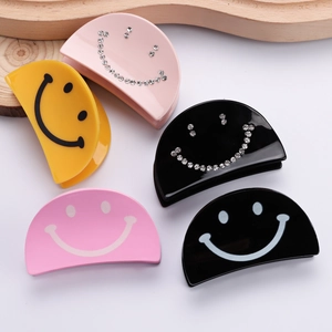 Five smiley face acrylic hair claws in yellow, pink and black with rhinestone details