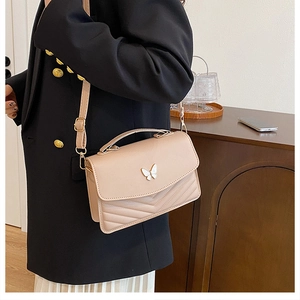 Detail of nude shoulder bag featuring V-shaped quilting and a golden butterfly clasp