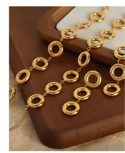 Detail of gold-plated titanium necklace with interlocking rings on wooden tray
