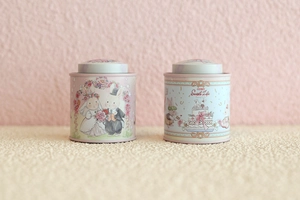 Pink and light blue bunny tin boxes with arched lids shown on a soft beige velvet surface